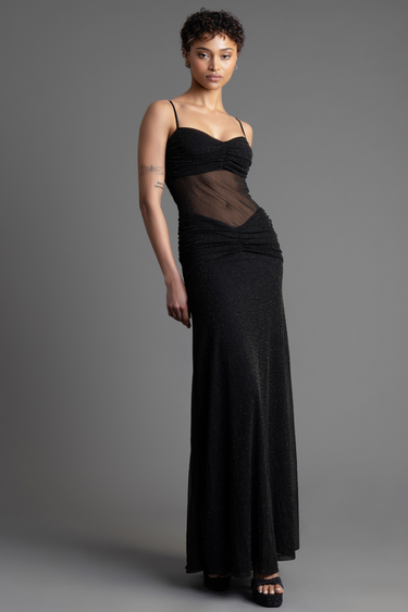 woman in a black glitter maxi dress with sheer midsection and ruched bodice, thin straps, and heels