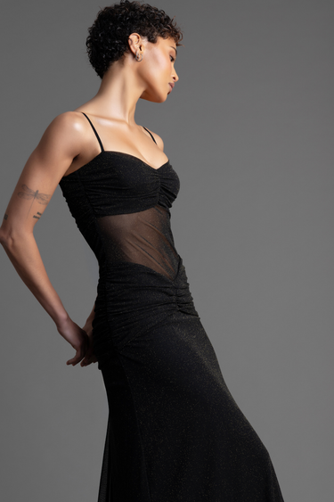woman wearing a black glitter maxi dress with a sheer midsection and ruched detailing, side profile