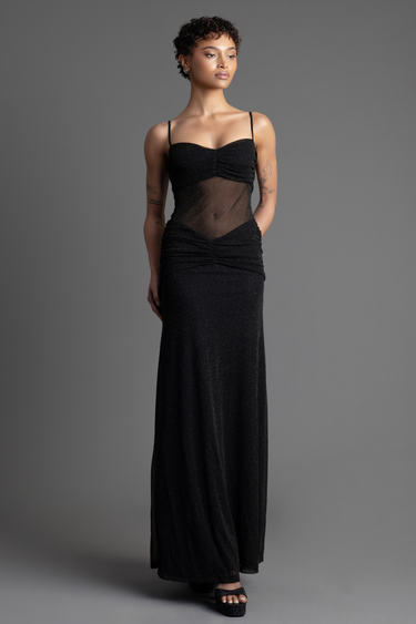 woman in a black glitter maxi dress with sheer midsection, ruched bodice, and thin straps, paired with black heeled sandals