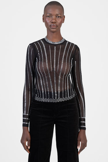 model wearing a sheer black long-sleeve top with white beadlike lines and a high neckline, paired with black pants