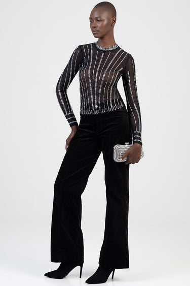 model wearing sheer black long sleeve top with white beaded stripes and high collar, black wide leg pants, black heeled
