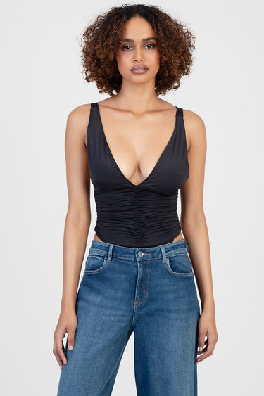 woman in a black ruched sleeveless bodysuit with a plunging neckline paired with blue jeans