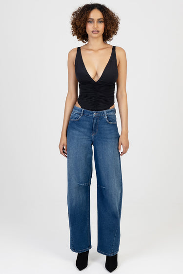 woman wearing a black ruched V neck sleeveless bodysuit and blue wide leg jeans