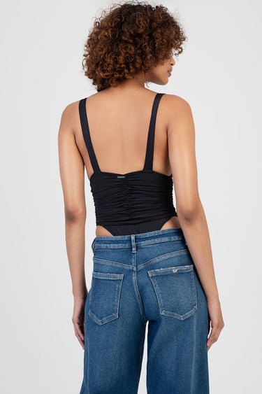 woman seen from behind in a black ruched sleeveless bodysuit with wide straps paired with blue jeans