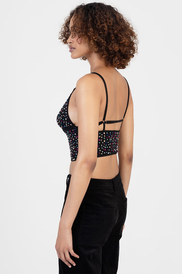 side view of a person wearing a black sequin crop top with thin straps and a wide back band, paired with black pants