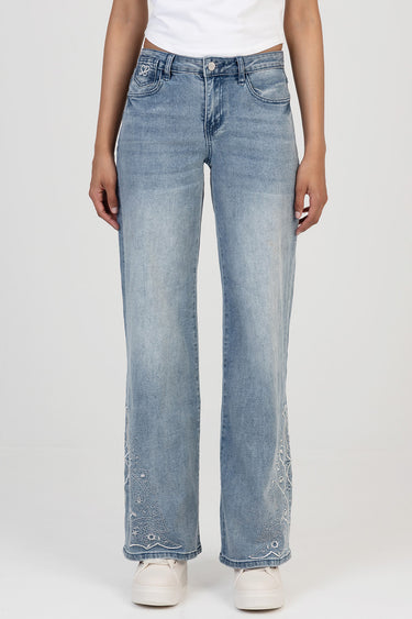 woman wearing light blue wide leg jeans with embroidered paisley patterns at the lower legs and white sneakers.