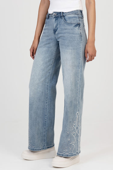 woman in light wash wide leg jeans with white embroidery along the lower right leg and white sneakers