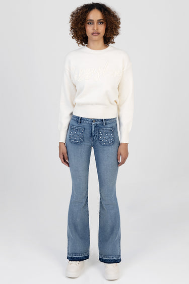 woman in cream sweater and Blue Jean Traders denim jeans with studded pockets and flare leg