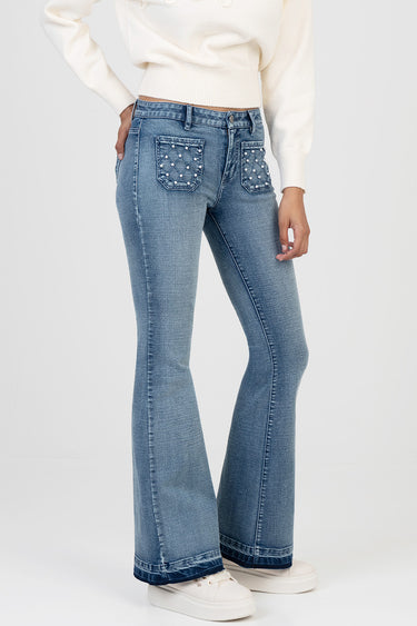 woman wearing light wash denim jeans with flare legs and quilted back pockets embellished with studs, paired with a white