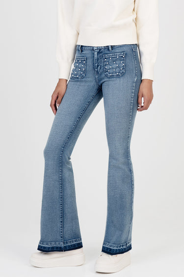 woman wearing light blue denim jeans with quilted back pockets and studs, flare leg opening, paired with a cream sweater