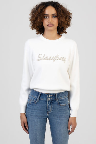 woman in white knit sweater with glittery script across the chest and blue jeans