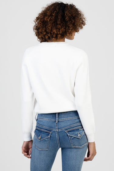 back view of a white knit sweater on a person with long sleeves, paired with blue denim jeans showing rear pockets