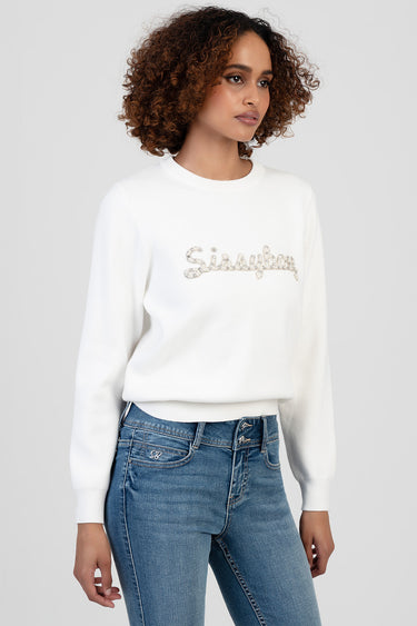 woman in white knit sweater with silver glitter script logo, blue jeans