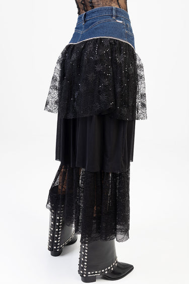 side view of a blue denim skirt with a black lace overlay and sequined hem, worn with black studded boots