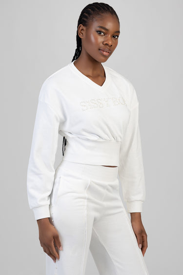 model wearing a white cropped sweatshirt with rhinestone lettering and high waist white pants with pearl accents