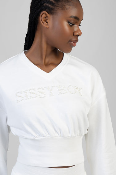 white cropped knit top with long sleeves and beaded logo across the chest