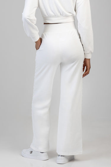 back view of a person wearing white wide leg pants with pearl bead trim along the outer seams, a matching white sweatshirt