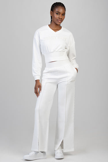 woman wearing a white cropped long sleeve sweatshirt with a gathered hem and matching high waist wide leg pants with pearl