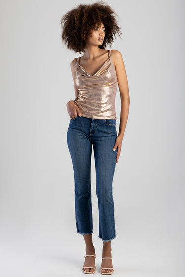 young woman wearing a rose gold metallic tank top with thin straps and a draped neckline, paired with blue denim jeans and