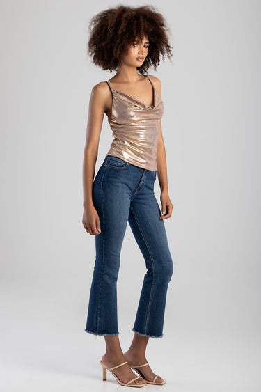 woman wearing a metallic rose gold sleeveless top with a draped neckline and ruched sides, paired with blue denim jeans and