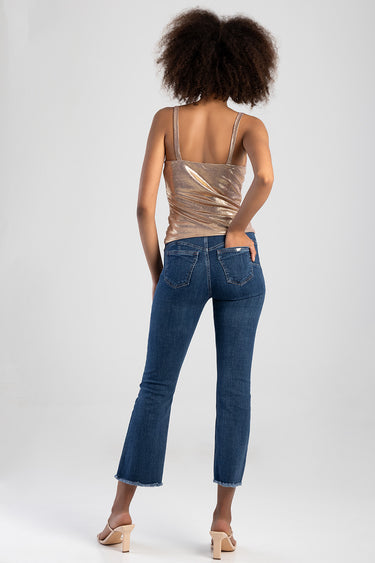 woman from behind wearing a rose gold metallic sleeveless top with thin straps and blue jeans with frayed hems and beige