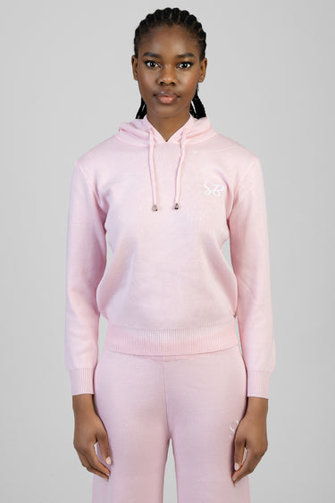 woman wearing a pastel pink knit hoodie with drawstrings and matching sweatpants, small white logo on the chest.