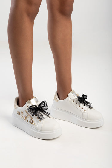 pair of white platform sneakers with black lace bows and scattered gold charms on the sides