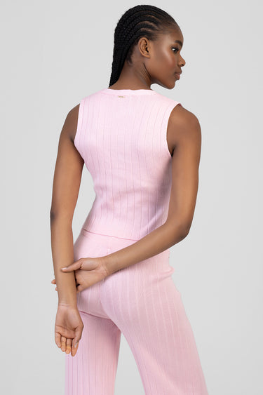 woman wearing a light pink ribbed knit sleeveless waistcoat and matching pants, seen from the back