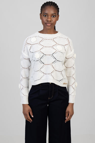 model wearing a white openwork knit sweater with circular stitch patterns and knitted flower patches, paired with black