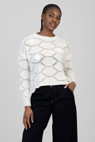 woman wearing white crochet knit sweater with floral appliques, paired with black pants