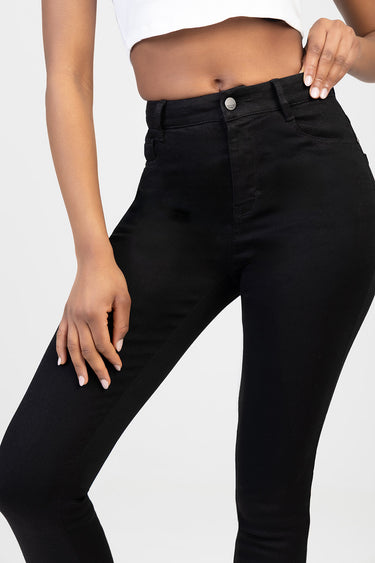 Black skinny jeans by Blue Jean Traders on a model with a cropped white top and a silver button at the waist.