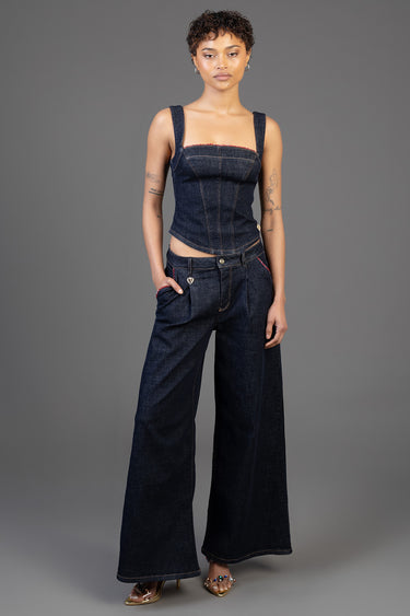 model wearing a dark denim corset top with wide straps and red trim, paired with wide-leg denim jeans and sandals