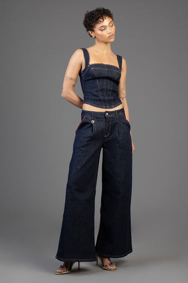 woman in a dark denim crop top and high waist wide leg jeans with red stitching, standing against a grey backdrop