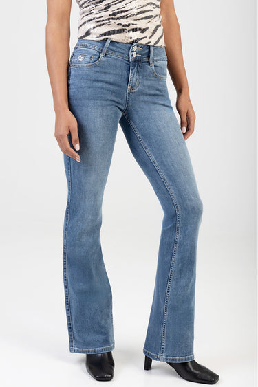 woman wearing blue bootleg jeans with faded front and five pockets, paired with a patterned top and black ankle boots