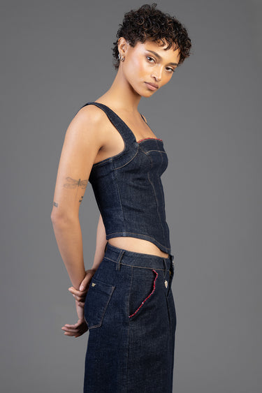 side view of a woman in a dark denim bustier top with wide straps and red trim at the neckline, paired with high waisted