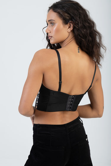 back view of a woman in a black corset top with lace-up back and rhinestone accents, paired with black jeans