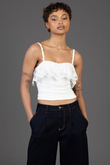 white lace crop top with a ruffled overlay and delicate straps, paired with dark wide leg pants