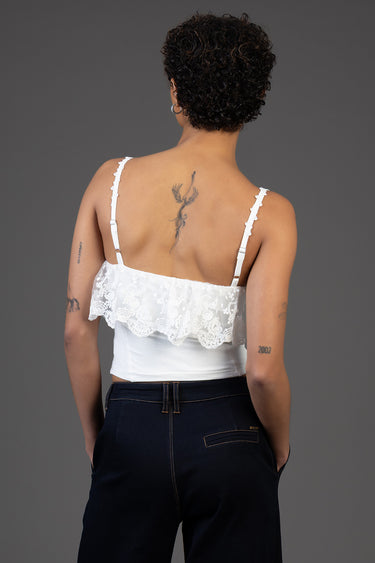back view of a person wearing a white lace cropped top with thin adjustable straps and dark jeans