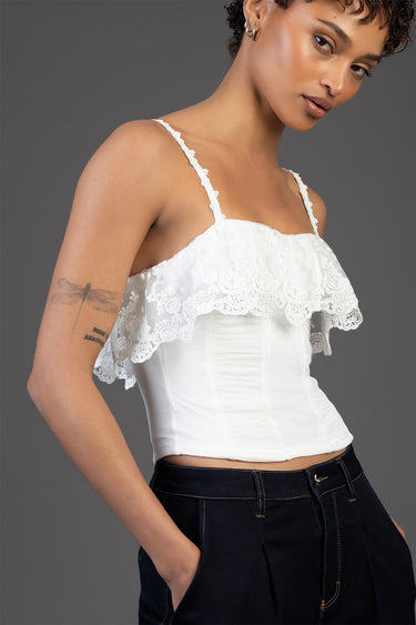 white lace trim sleeveless top with a ruffled neckline and thin straps, worn with dark denim pants