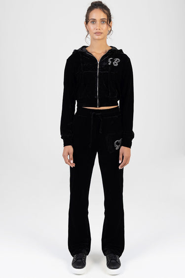 woman in black velour zip hoodie and matching joggers with a small logo on chest and leg, wearing black sneakers