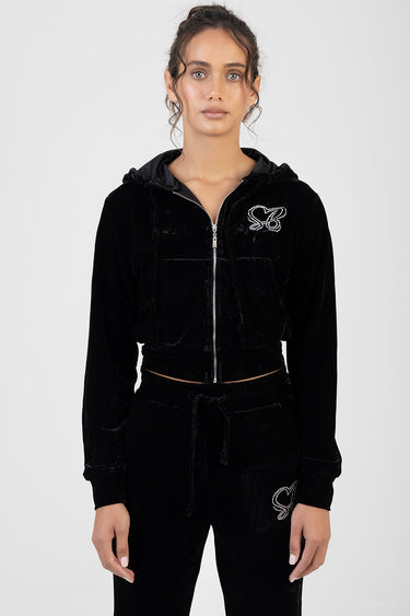 woman in black velour track top with hood and zip, butterfly rhinestone logo on chest, matching velour pants with drawstring