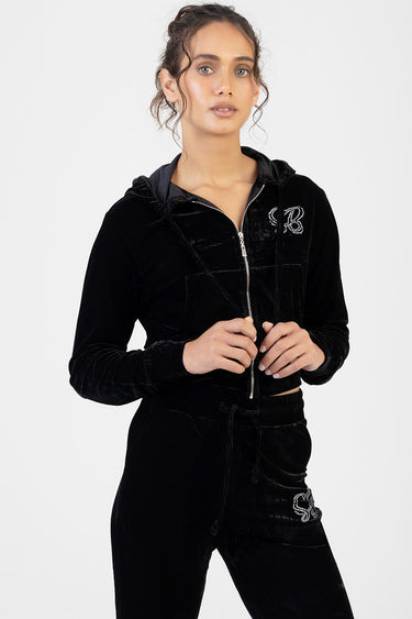 woman wearing a black velour zip hoodie with a drawstring hood and matching velour track pants with rhinestone logo details