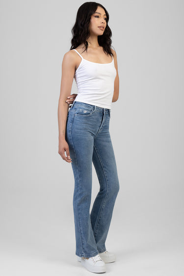woman in light blue bootleg jeans and a white tank top, standing in profile with white sneakers
