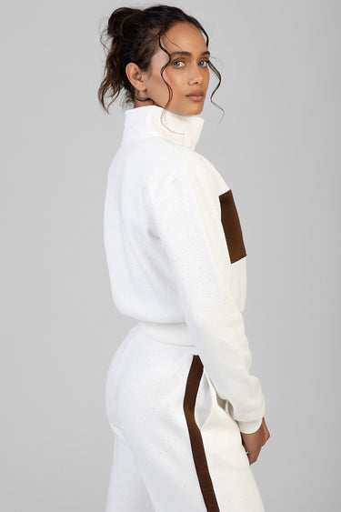 side view of a woman wearing a white speckled track top with a brown chest panel and matching pants