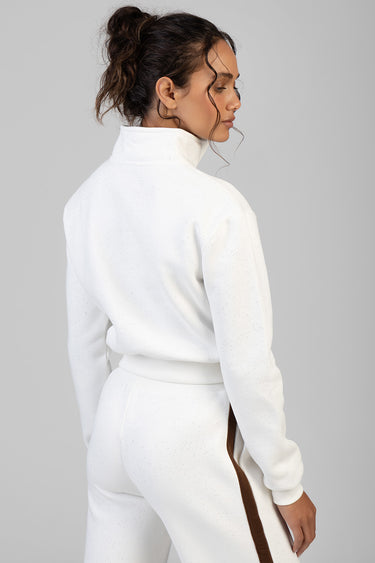 woman wearing white speckled high neck sweatshirt and matching pants with brown side stripe, back view