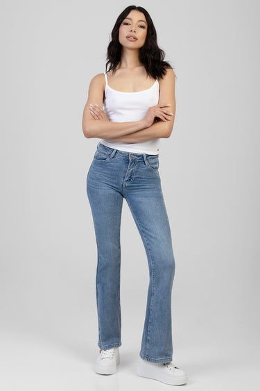 woman in a white tank top and light blue bootleg jeans with white sneakers, standing against a plain grey background