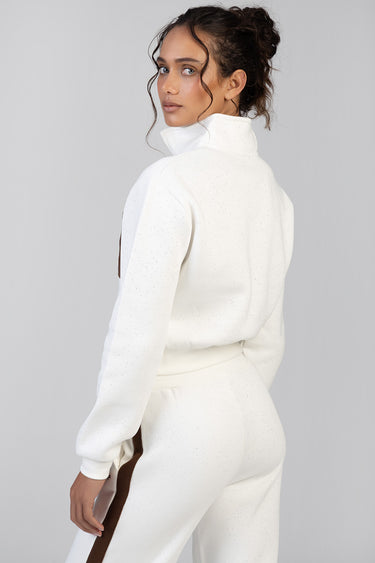 woman in a white speckled fleece track top with a high collar and matching pants with a brown side stripe