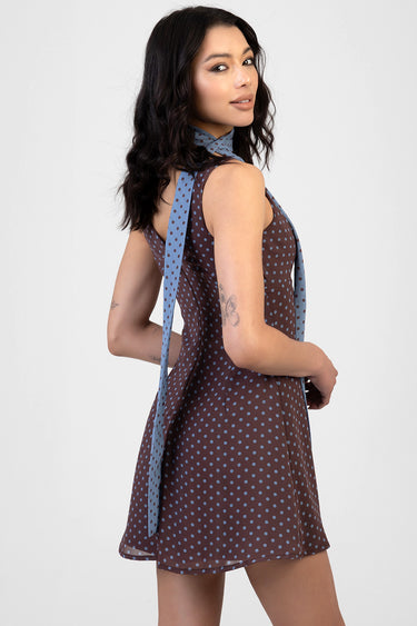 model in a brown polka dot sleeveless mini dress with a light blue scarf tied around the neck