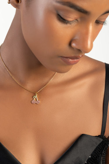 woman wearing a gold chain necklace with a cherry pendant encrusted with pink stones