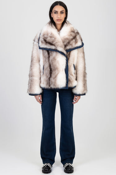 woman wearing a cream and brown faux fur jacket with navy edging, paired with dark denim flared jeans and embellished shoes